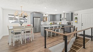 A modern kitchen with a central island, stainless steel appliances, and a dining area with white chairs.