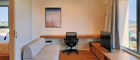 A modern office space with a sofa, a desk, a chair, a television, and a large window with a view.