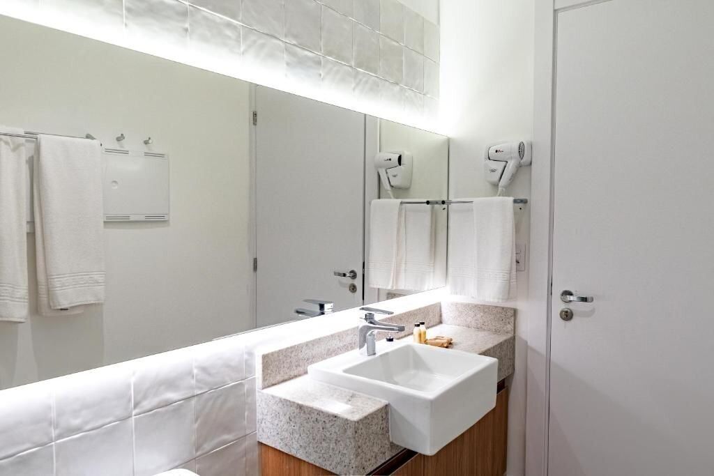 A modern bathroom with a large mirror, white sink, and towel racks.