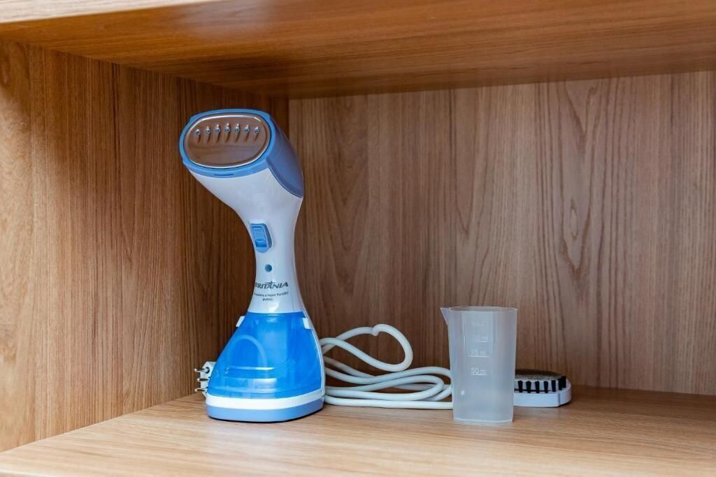 Een blauw-witte haardroger op een houten plank met een maatbeker en een borstel.