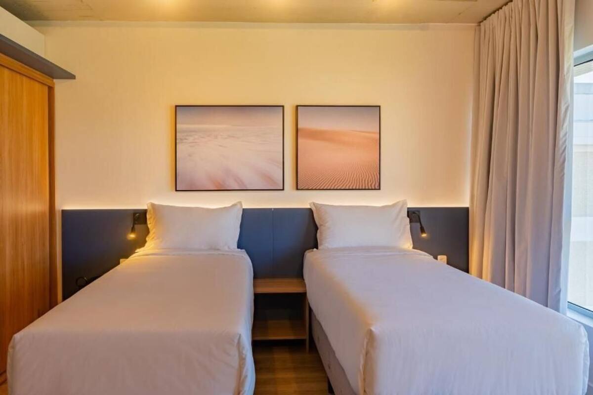 Habitación de hotel con dos camas individuales, un armario de madera, una mesita de noche y dos cuadros en la pared.