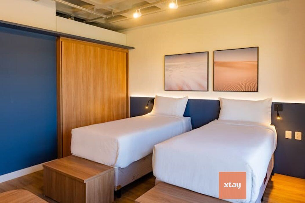A hotel room with two single beds, a wooden wardrobe, and two framed pictures on the wall.