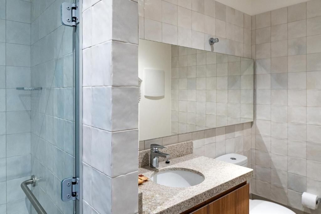 Un baño moderno con cabina de ducha de vidrio, lavamanos con espejo e inodoro.