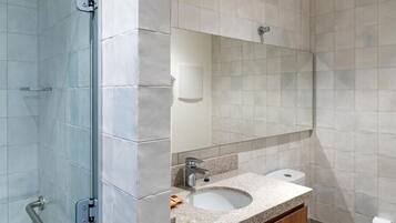 Un baño moderno con cabina de ducha de vidrio, lavamanos con espejo e inodoro.
