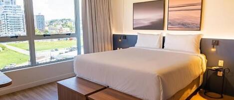 A modern hotel room with a large bed, a view of the city, and a small side table.