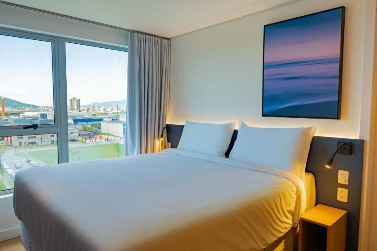 Habitación de hotel con una cama grande, vistas de la ciudad a través de la ventana y un cuadro en la pared.