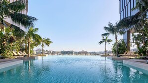 Ein Swimmingpool mit Liegestühlen und Palmen, umgeben von modernen Gebäuden.