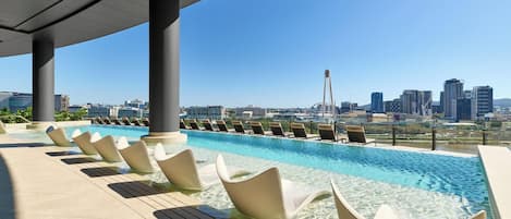 A rooftop pool with lounge chairs and a cityscape view.
