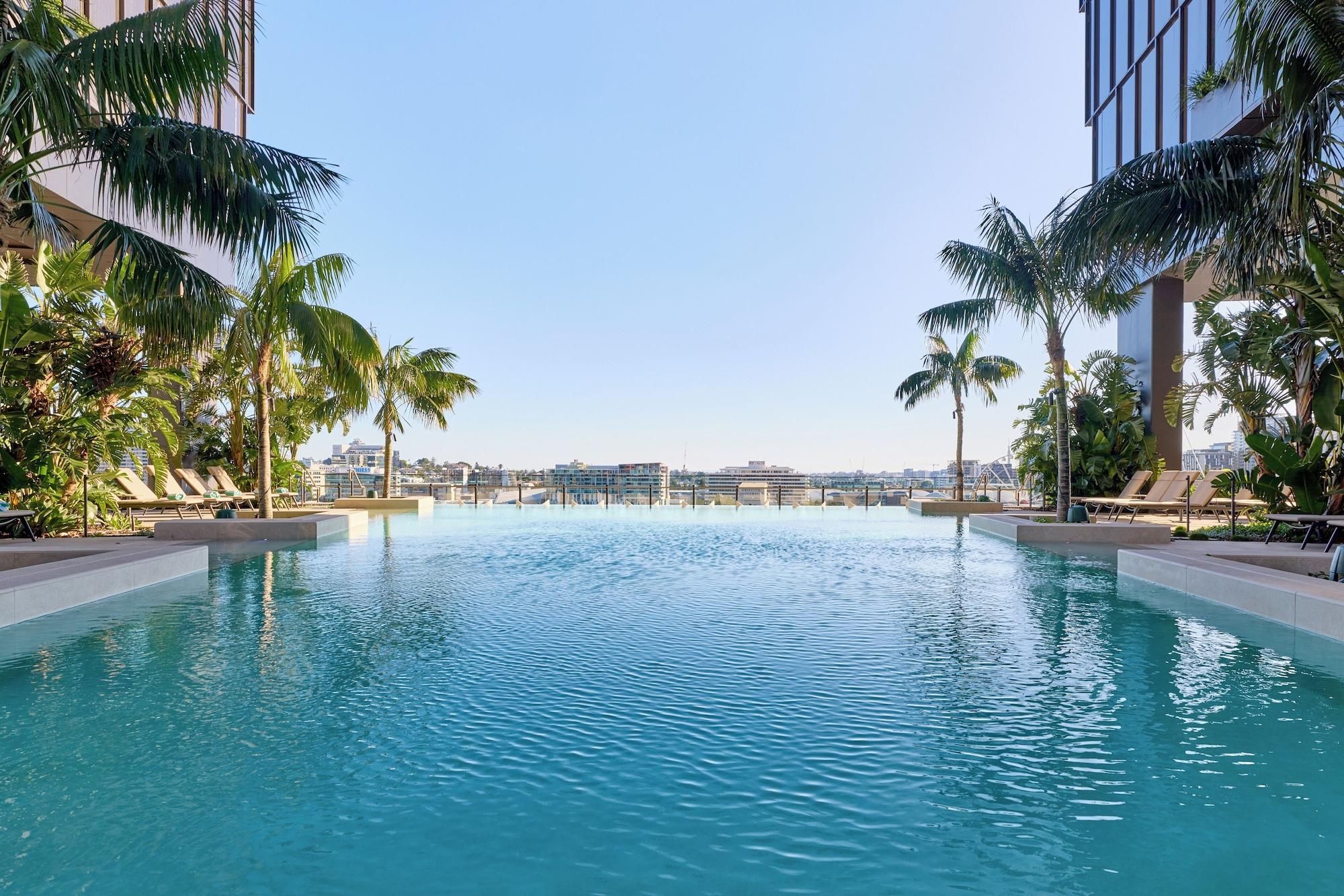 A swimming pool with lounge chairs and palm trees, surrounded by modern buildings.