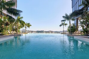 Ein Swimmingpool mit Liegestühlen und Palmen, umgeben von modernen Gebäuden.