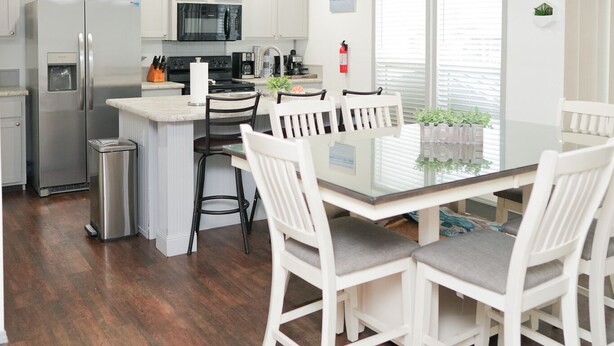 A modern kitchen with white cabinetry, stainless steel appliances, and a dining area with white chairs and a glass table. - ☀️WATERFRONT W BOAT ACCESS PCB. 3BD 2BA. PRIVATE CANAL RIGHT TO THE BAY (Panama City Beach)