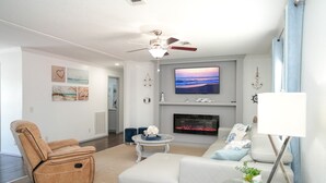 A modern living room with a fireplace, a reclining chair, a flat-screen TV, and a ceiling fan. - ☀️WATERFRONT W BOAT ACCESS PCB. 3BD 2BA. PRIVATE CANAL RIGHT TO THE BAY (Panama City Beach)