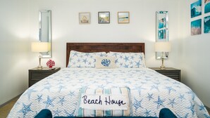 A bedroom with a bed featuring a starfish pattern, a headboard, and a pillow labeled "Beach House". There are wall-mounted lamps and framed pictures above the bed. - ☀️WATERFRONT W BOAT ACCESS PCB. 3BD 2BA. PRIVATE CANAL RIGHT TO THE BAY (Panama City Beach)