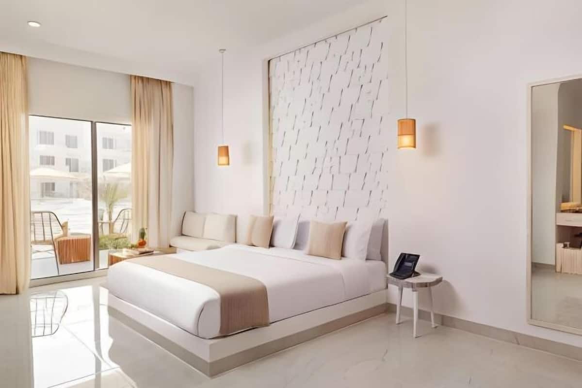 Habitación de hotel moderna con una cama grande, una mesita de noche pequeña, un espejo y vistas al exterior.