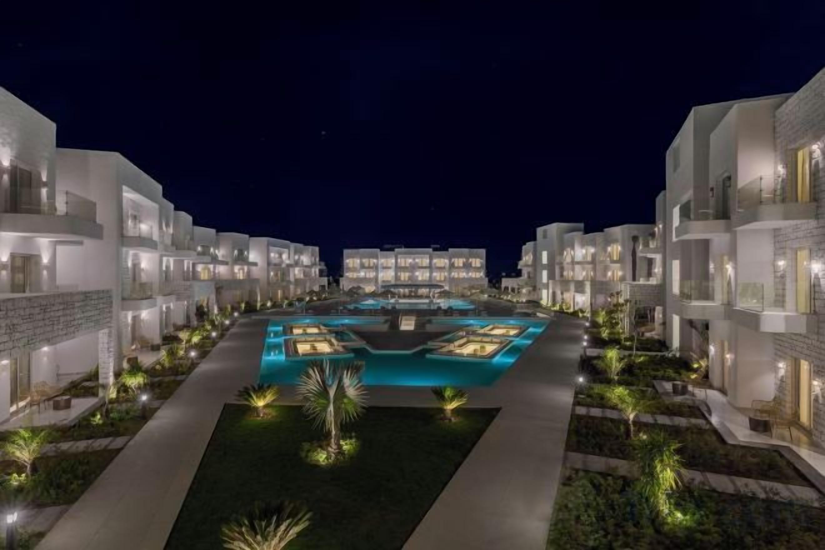Un hotel con varias edificaciones, una piscina central y senderos bien iluminados.