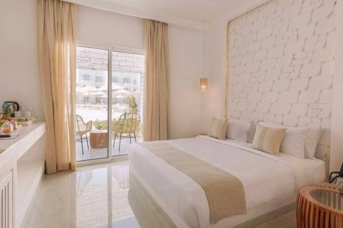 Habitación de hotel con una cama grande, una puerta de vidrio que da a un espacio exterior, una pared con diseño de ladrillo y una pequeña mesa redonda.