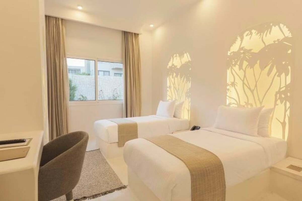 Une chambre d’hôtel avec deux lits, un bureau, une chaise et une fenêtre avec des rideaux.