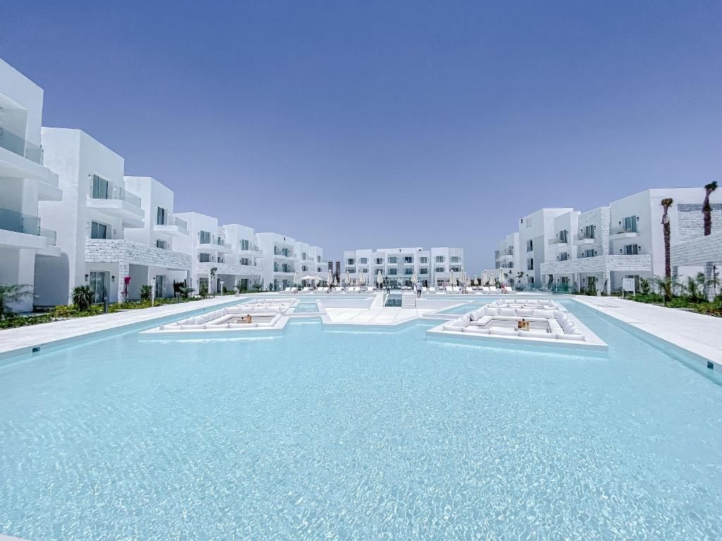 A modern hotel with a central swimming pool, white buildings, and a clear sky.