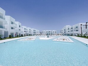 Un hôtel moderne doté d’une piscine centrale, de bâtiments blancs et offrant une vue sur un ciel dégagé.
