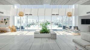 Un vestíbulo amplio con un gran muro de cristal, una planta central y zonas de estar.