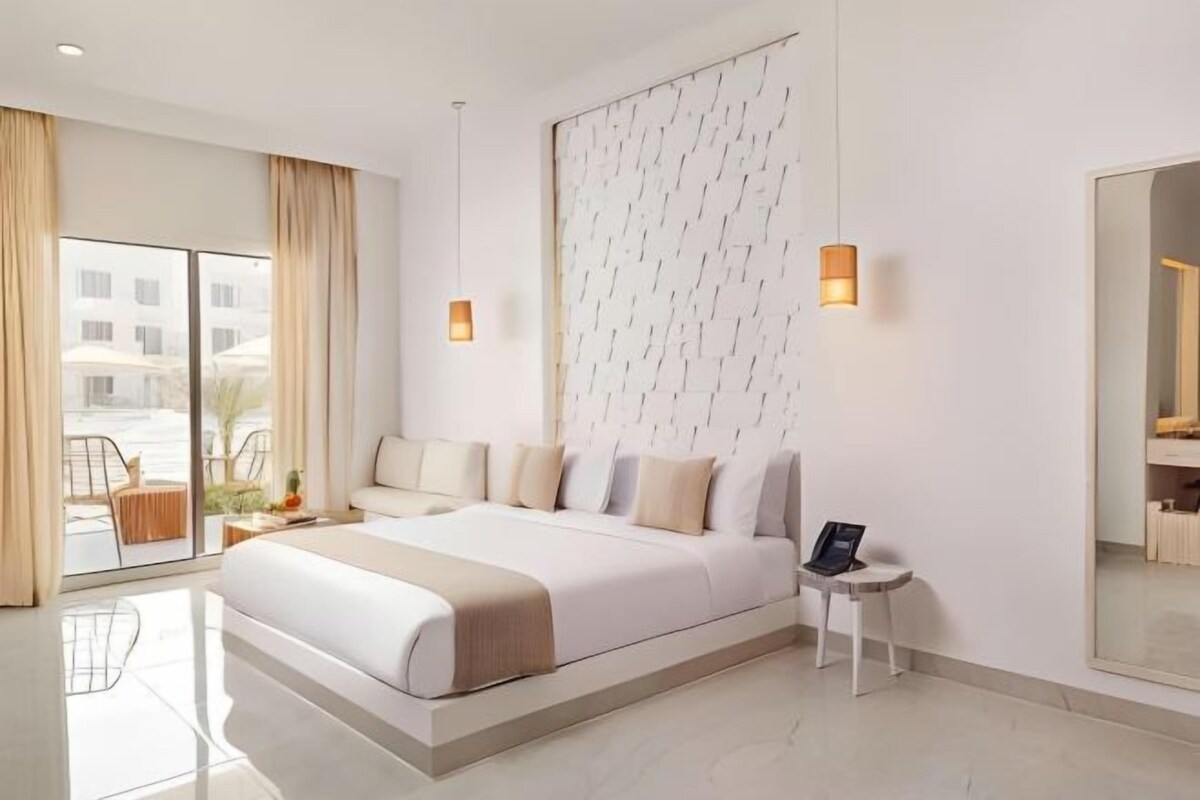 Ein modernes Hotelzimmer mit einem großen Bett, einem kleinen Nachttisch, einem Spiegel und Blick nach außen.