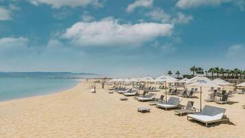 A beach with sun loungers and umbrellas, a clear sky, and a calm sea.