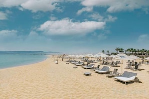 A beach with sun loungers and umbrellas, a clear sky, and a calm sea.