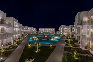 Un hotel moderno con piscina central, rodeado de senderos iluminados y vegetación.