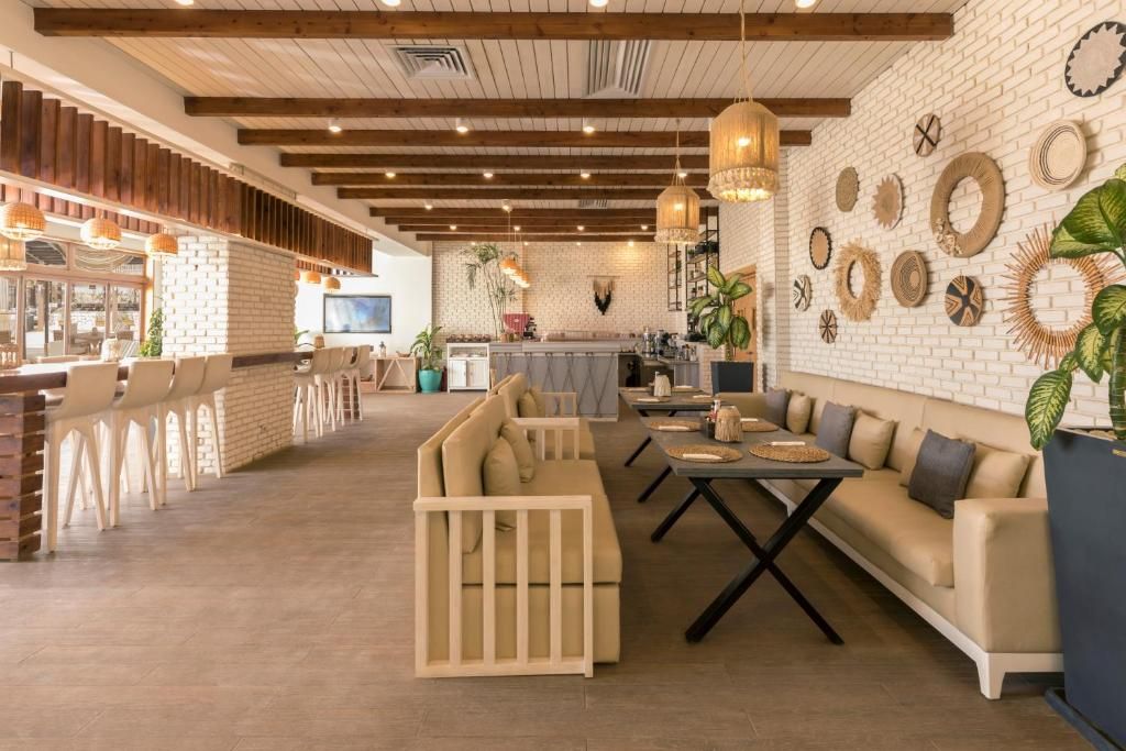 A spacious lounge area with a long wooden bench, a sofa, and a dining table. There is a kitchen area in the background with a bar and various decorative items on the wall.
