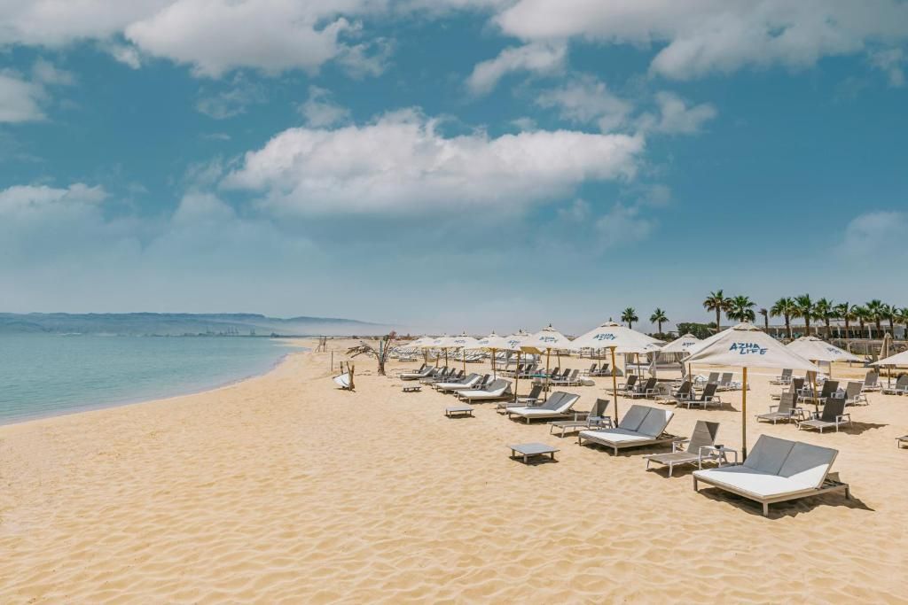 A beach with sun loungers and umbrellas, a clear sky, and a calm sea.