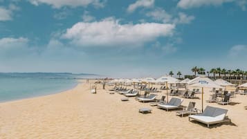 A beach with sun loungers and umbrellas, a clear sky, and a calm sea.