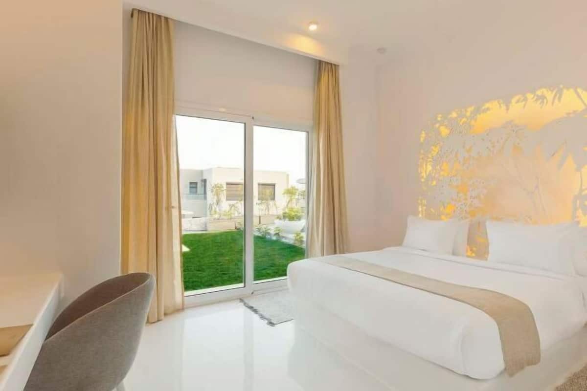 Una habitación de hotel moderna con una cama grande, un escritorio y vistas a un césped verde y edificios.