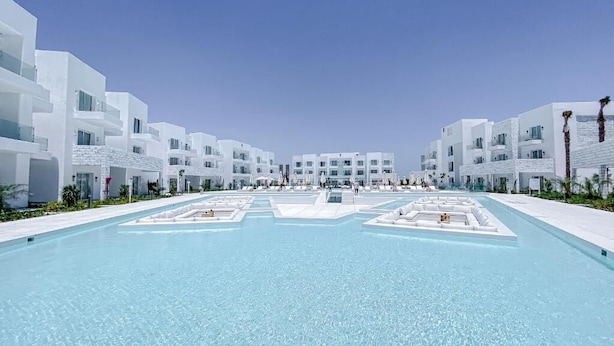 Un hotel moderno con piscina central, edificios blancos y cielo despejado.
