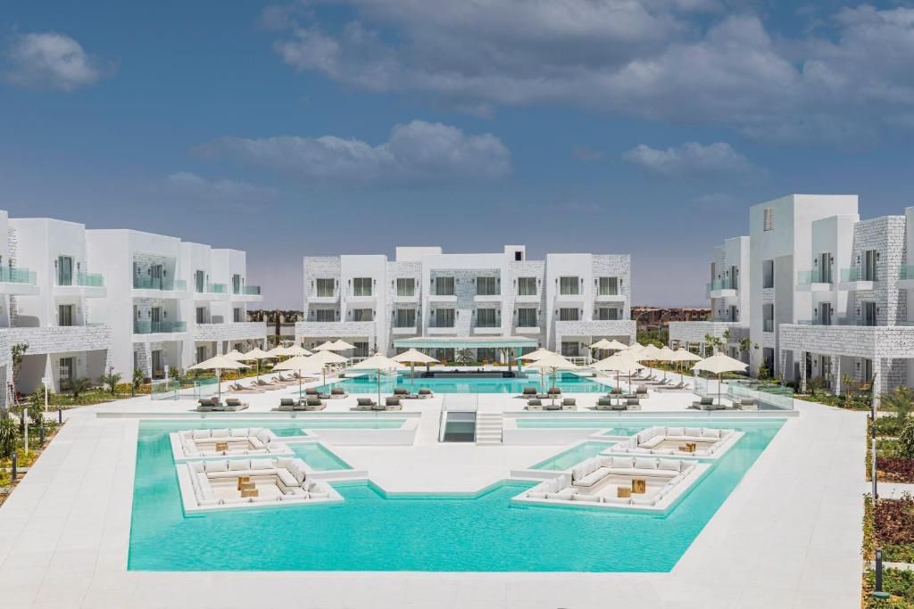 Un hotel moderno con piscina central, varias zonas de descanso y cielo despejado.