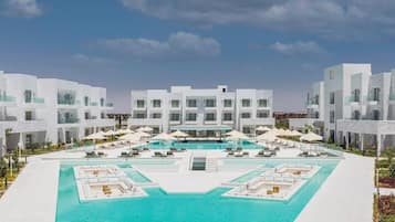 A modern hotel with a central swimming pool, multiple lounge areas, and a clear sky.