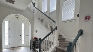 A spacious interior with a grand staircase, white walls, and a doormat with a shoe removal request.