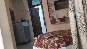 A room with a bed, a ceiling fan, a TV on a shelf, and a door leading to another room.