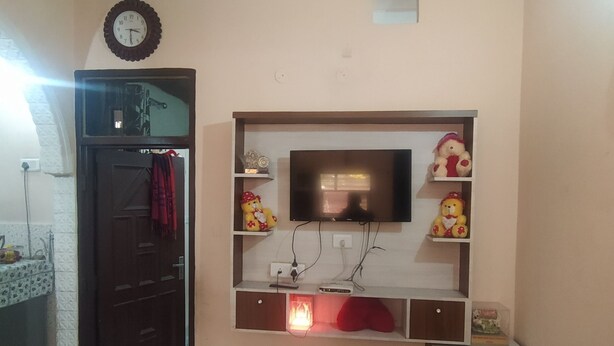 A living room with a television mounted on a wall, a clock, and a small cabinet.