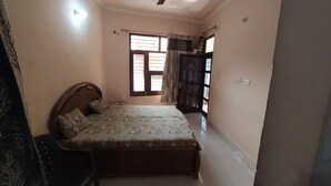 A bedroom with a bed, a chair, a window with curtains, and a door.