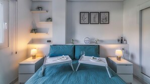 A bedroom with a bed, two bedside tables, a nightstand, a shelf with plants, and wall art. - Stunning Ground Floor Apartment (Sucina)