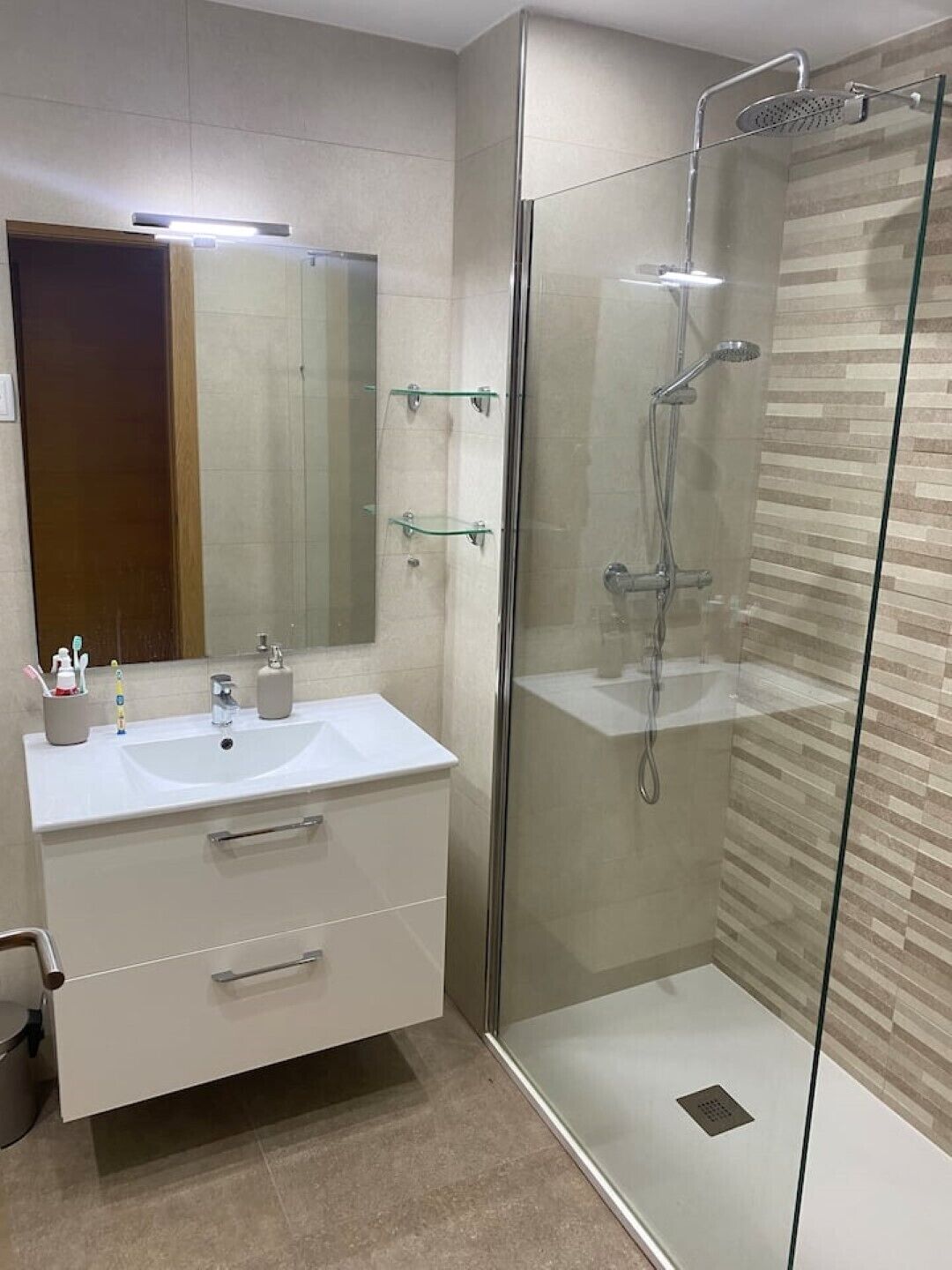 A modern bathroom with a glass-enclosed shower, a white vanity with a mirror, and a tiled floor.