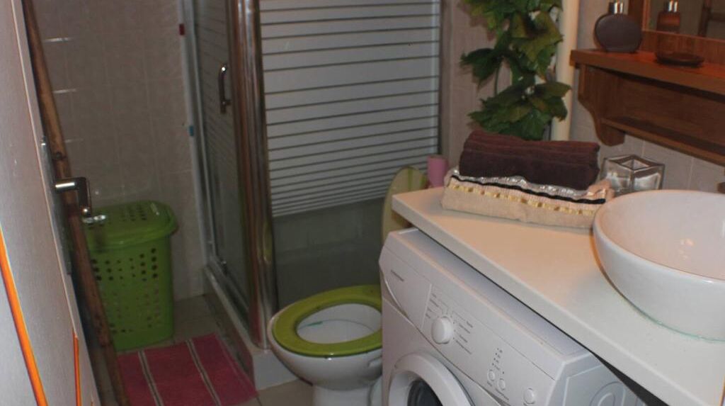 Pieni kylpyhuone, jossa on vihreä wc-istuin, pesukone ja pesuallas.