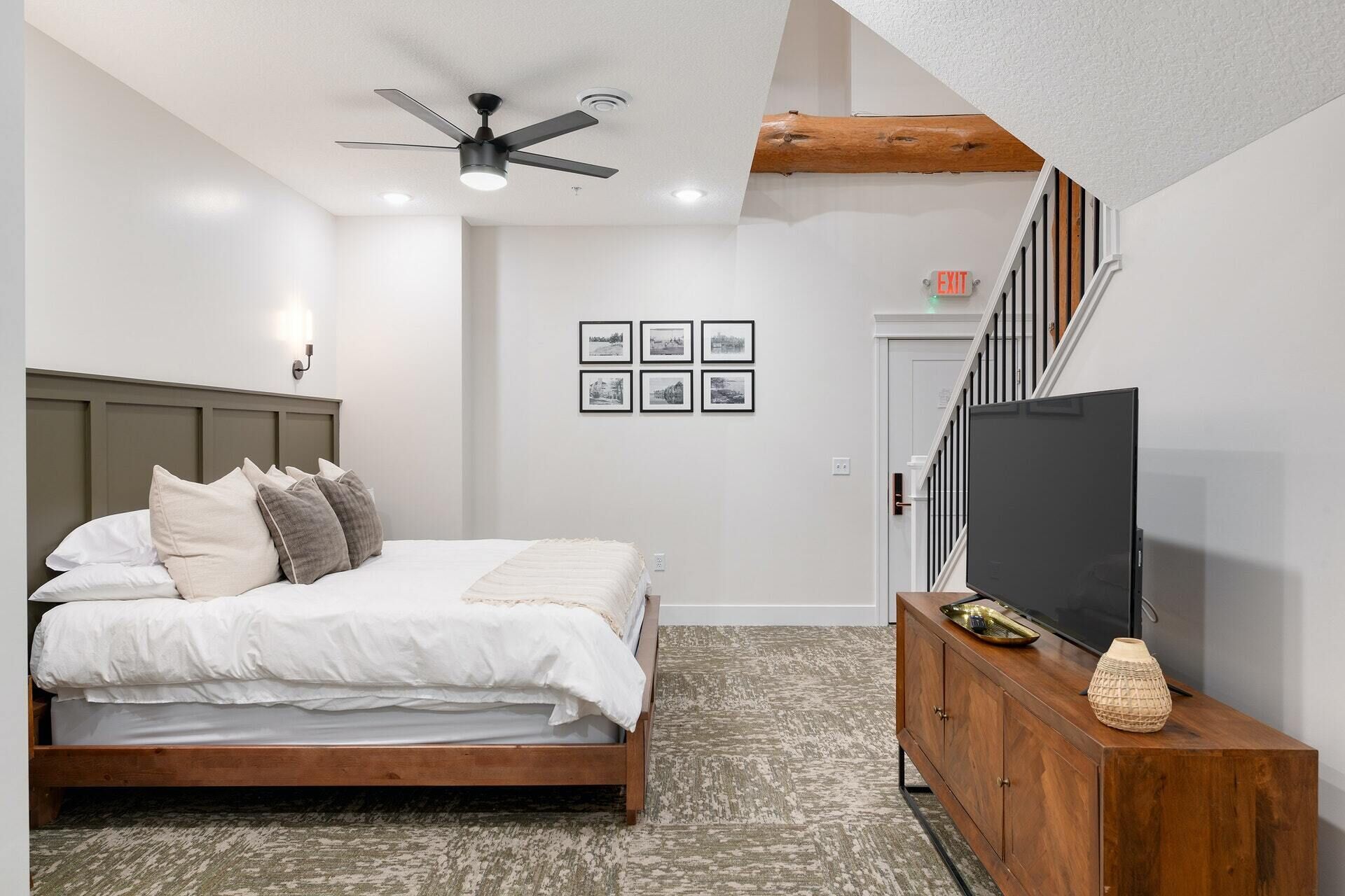 Un dormitorio con cama, ventilador de techo, televisión y cómoda de madera.