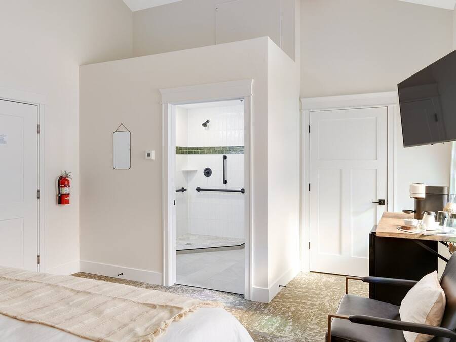 Habitación de hotel con cama, escritorio con silla, televisor y zona de ducha.