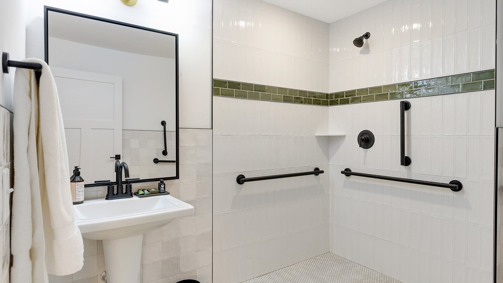A bathroom with a white sink, mirror, and a shower area with grab bars.