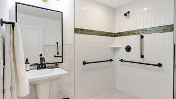 A bathroom with a white sink, mirror, and a shower area with grab bars.