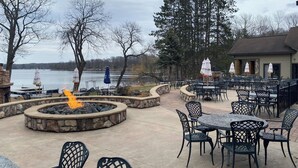 An outdoor patio with stone seating, tables, and chairs, overlooking a lake. - Balsam Lake Lodge (Balsam Lake)