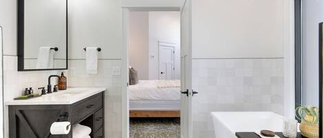 A modern bathroom with a large mirror, a sink with toiletries, a bathtub, and a shower area.