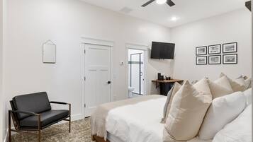 A bedroom with a bed, a chair, a desk with a coffee maker, a TV, and framed pictures on the wall.
