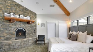 A bedroom with a stone fireplace, a bed with multiple pillows, a chair, and a window with a view. - Balsam Lake Lodge (Balsam Lake)